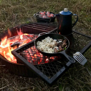 Rice and meat in a cast iron skillet are pictured above a campfire
