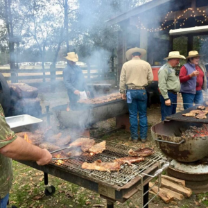 Cowboys stand beyond a smoking BBQ